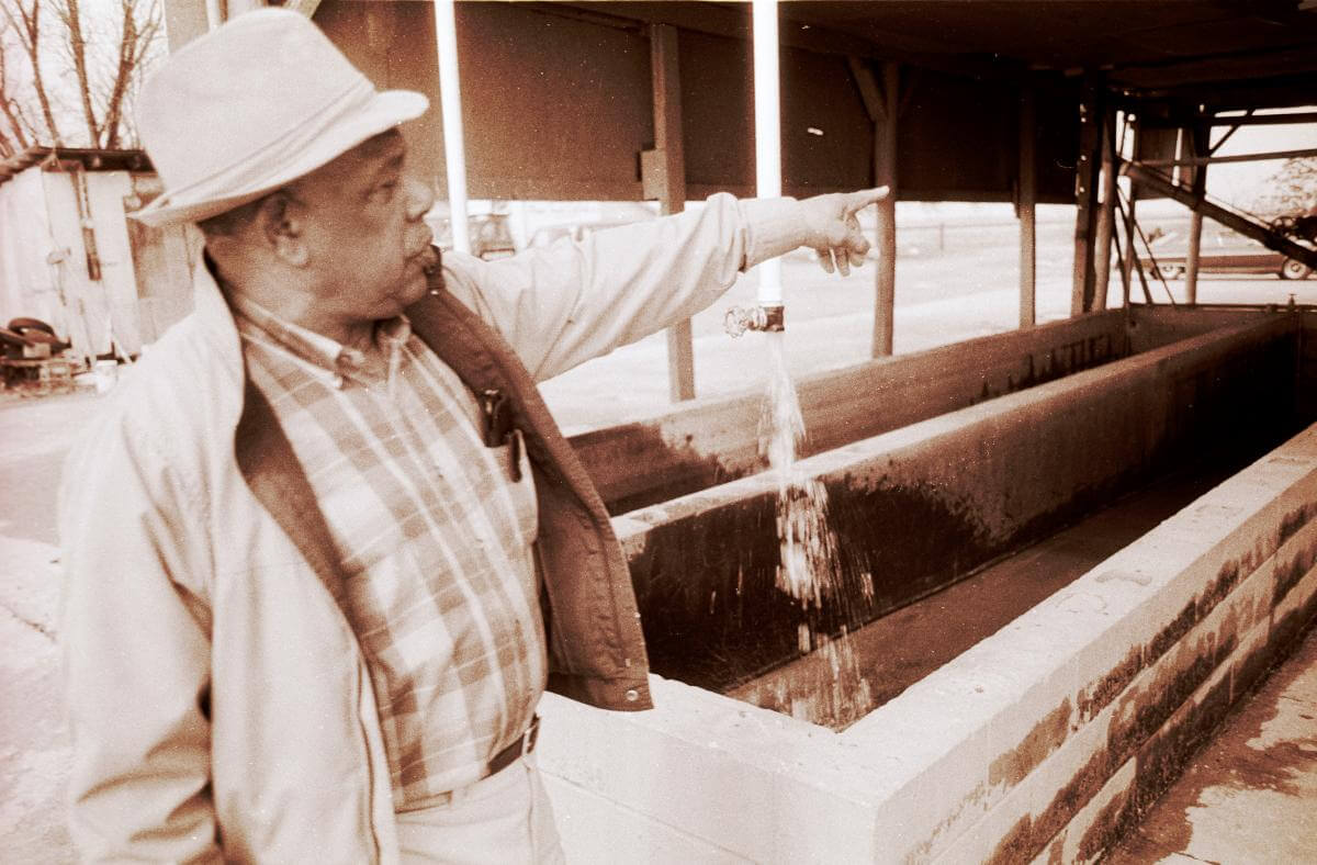 Ed Scott at his catfish processing plant, Leflore County, Mississippi, ca. 1985. Photograph by Lynn Marshall-Linnemeier. © Lynn Marshall-Linnemeier. A sepia-toned photograph of Ed Scott at his catfish processing plant, pointing to something outside the frame