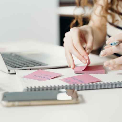 person writing on a pink sticky note