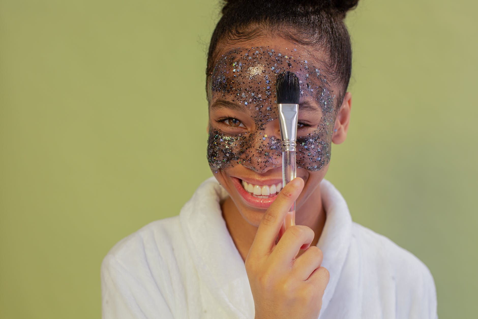 happy black teen applying exfoliating mask on face with applicator