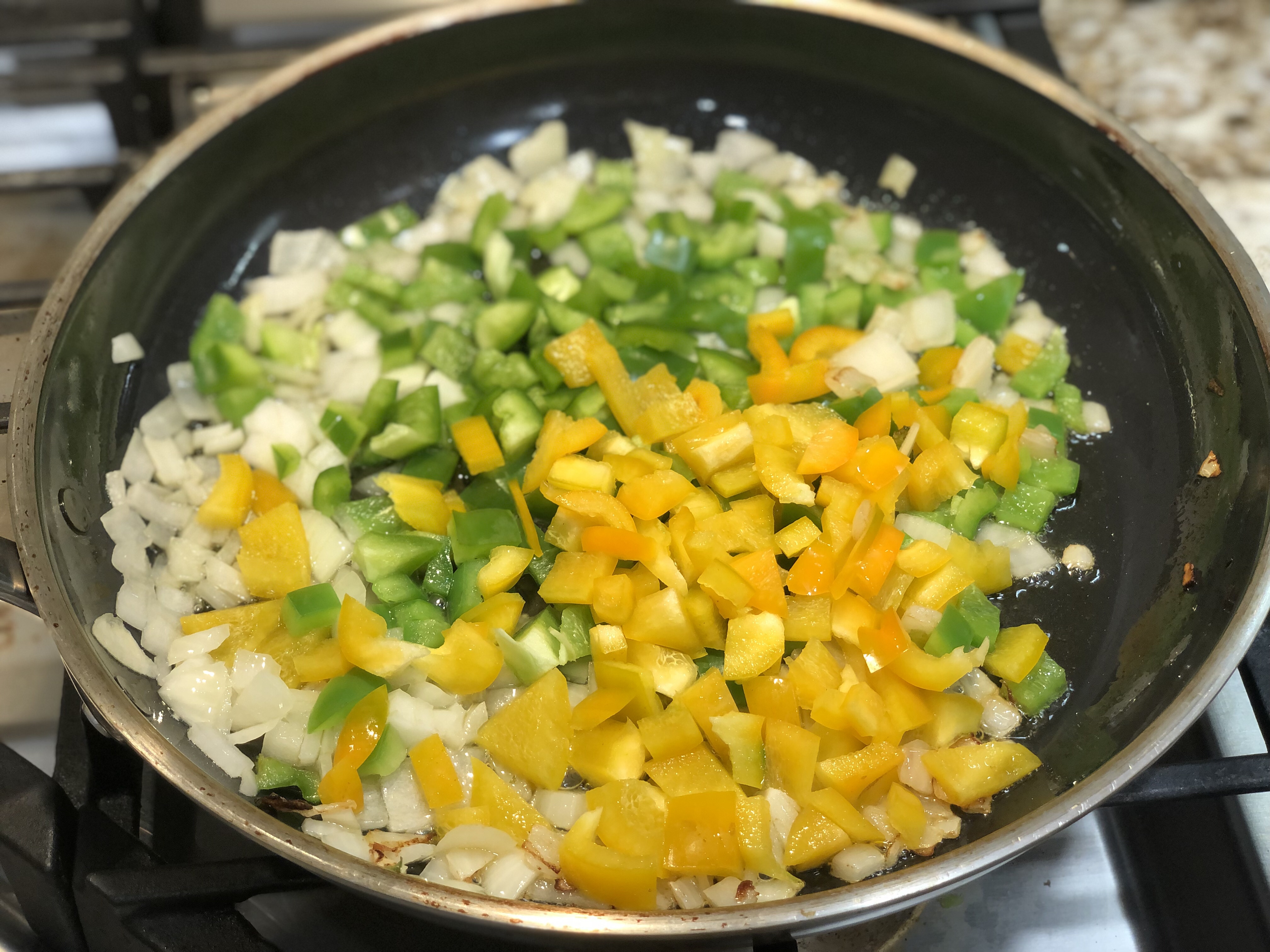 saute pan with diced yellow and green peppers and white onions