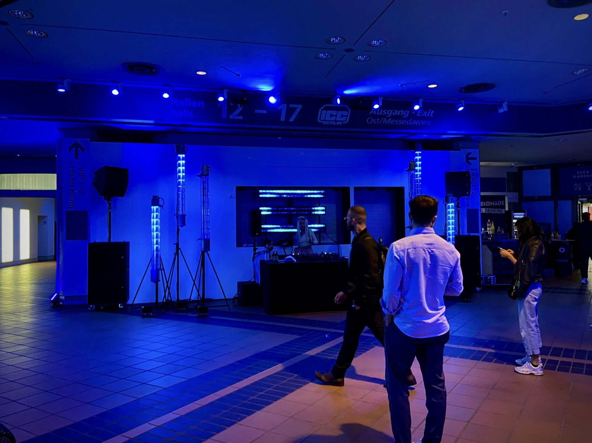Indoor-Event mit blauer Beleuchtung, Bühne, DJ und Teilnehmern in modernem Ambiente.