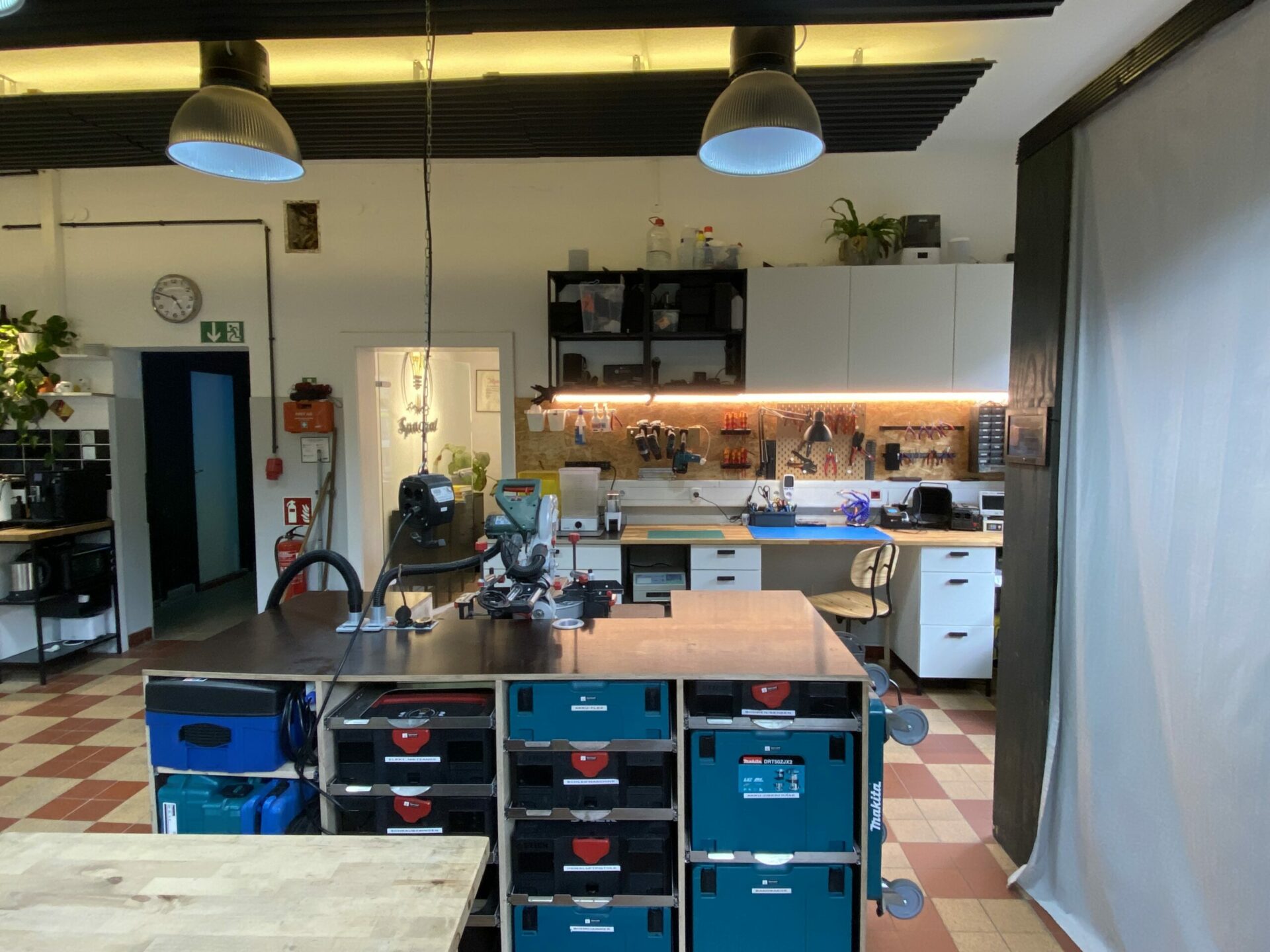 Gut organisierte Werkstatt mit warmen Farben, großem Holztisch, Werkzeugkästen und Pflanzen.