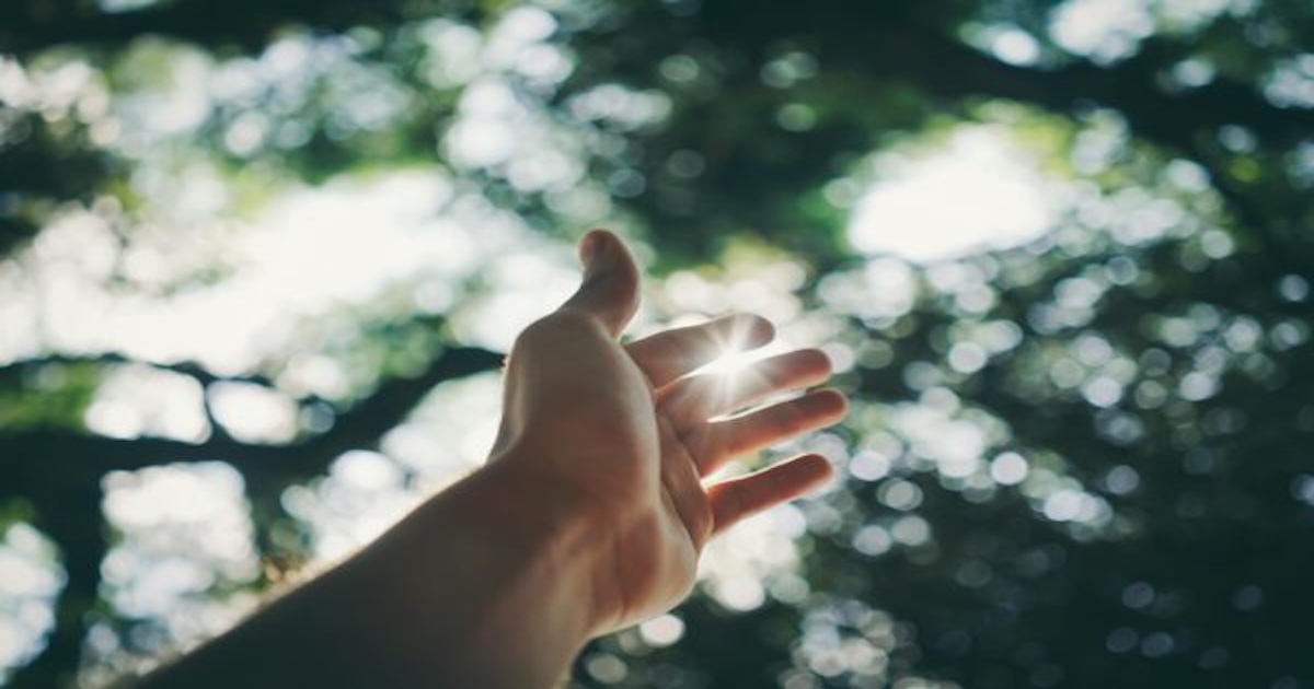 “A single hand lifted with light shining through the fingers, symbolizing God’s love and compassion shining through us.”