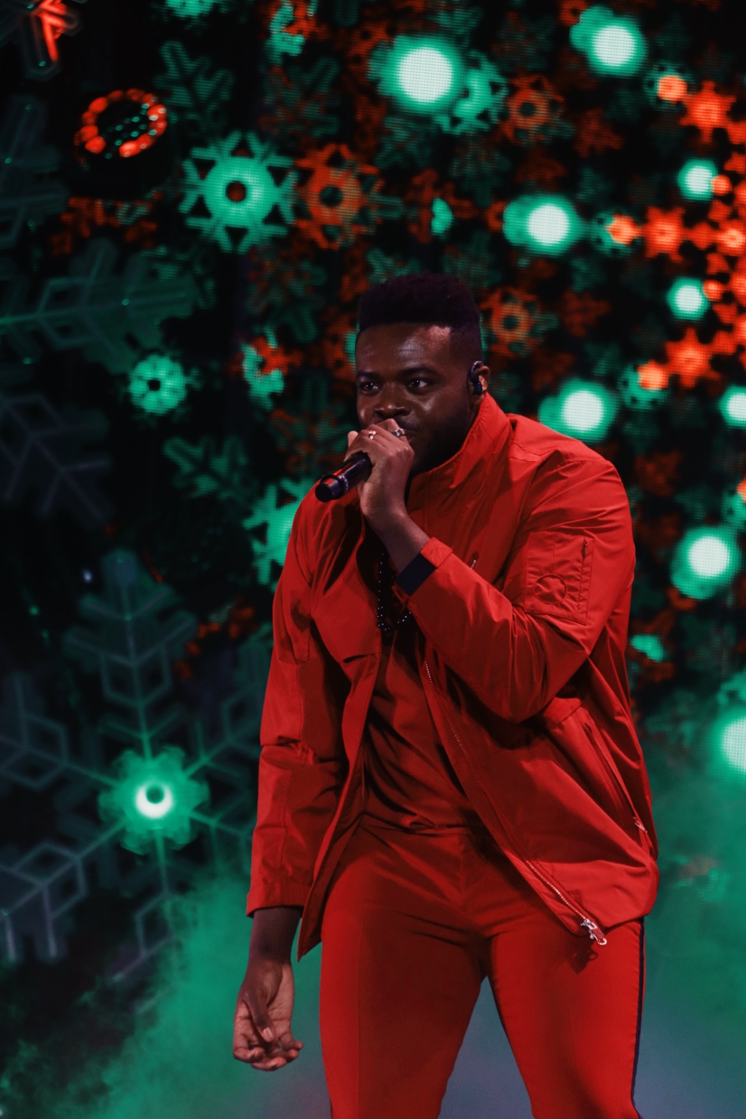 Kevin from Pentatonix singing on stage in a red jacket.