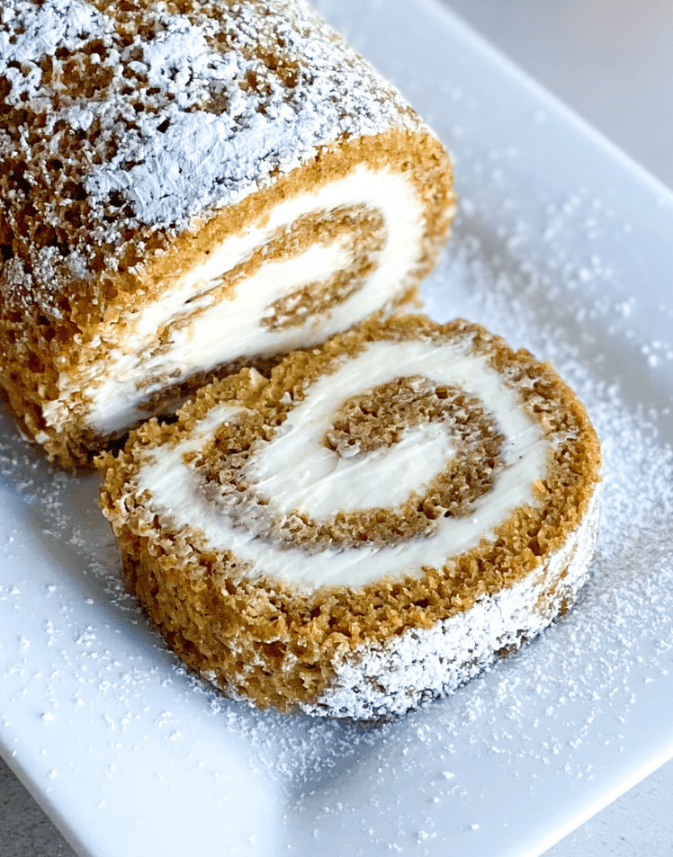 Pumpkin roll on platter with a small pumpkin on each side of pumpkin roll.