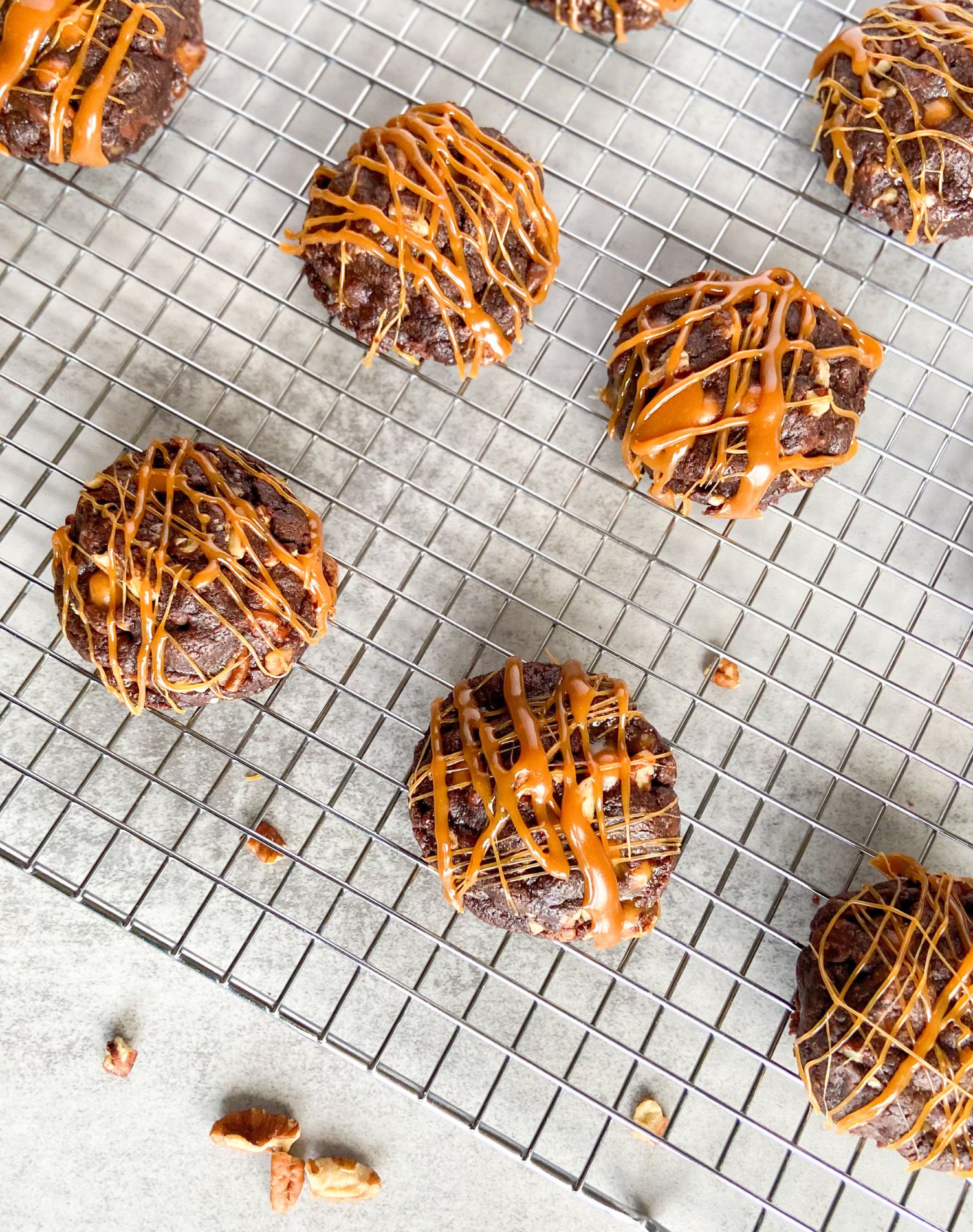 Cookies drizzled in caramel on a cooling rack with pecans scattered under rack.