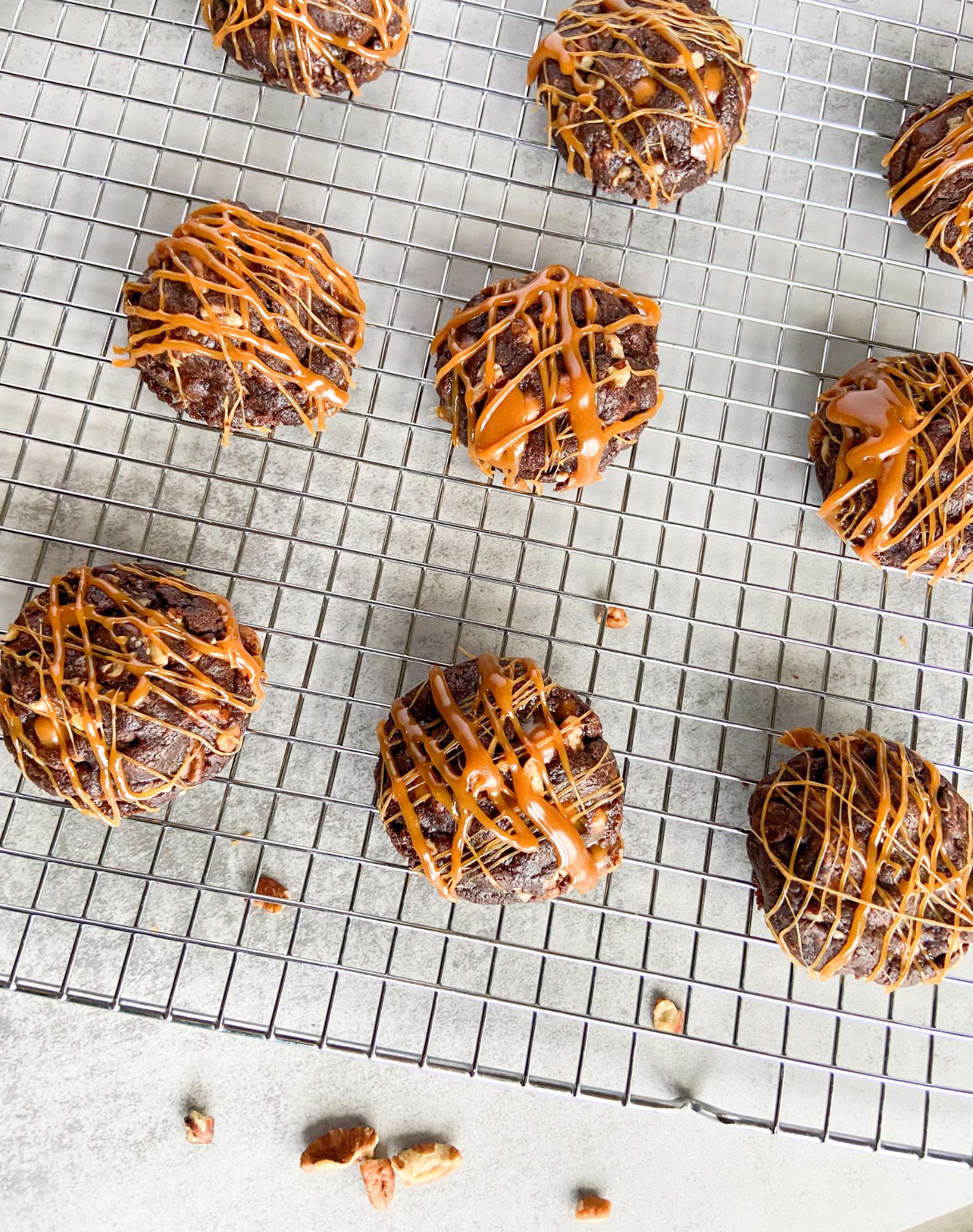 Cookies drizzled in caramel on a cooling rack with pecans scattered under rack.