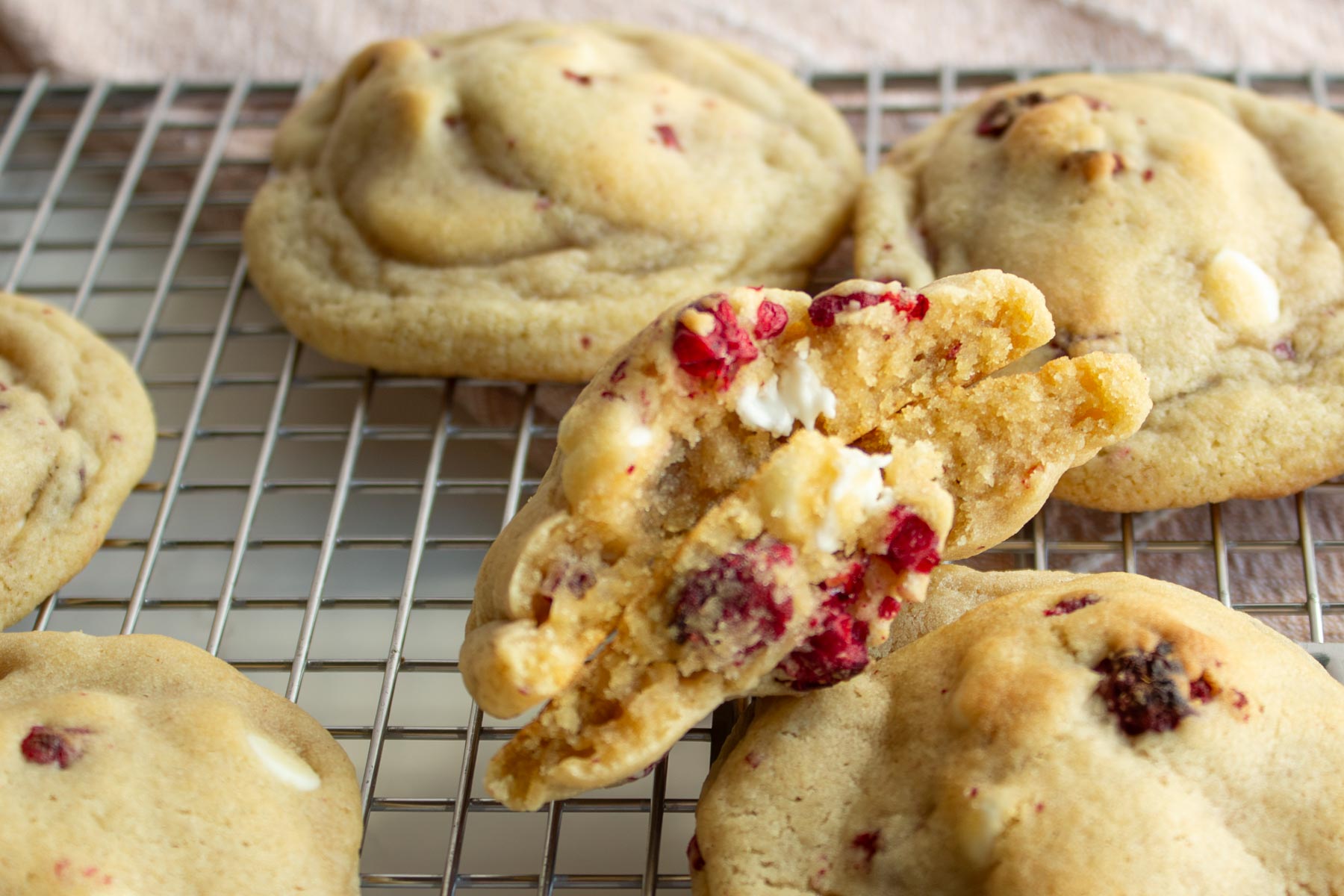 Soft white chocolate raspberry cookies with freeze-dried raspberries displayed on wire cooling rack.