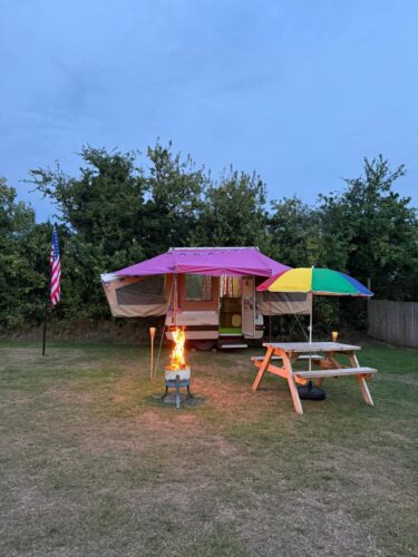 Our American camper Daisy at night time with outside picnic bench and firepit