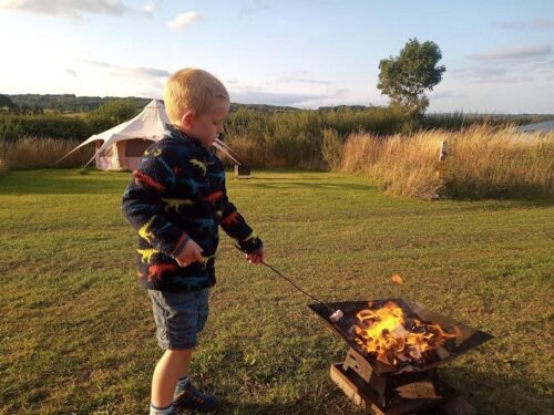 A child is tasting his marshmallow on a camp fire
