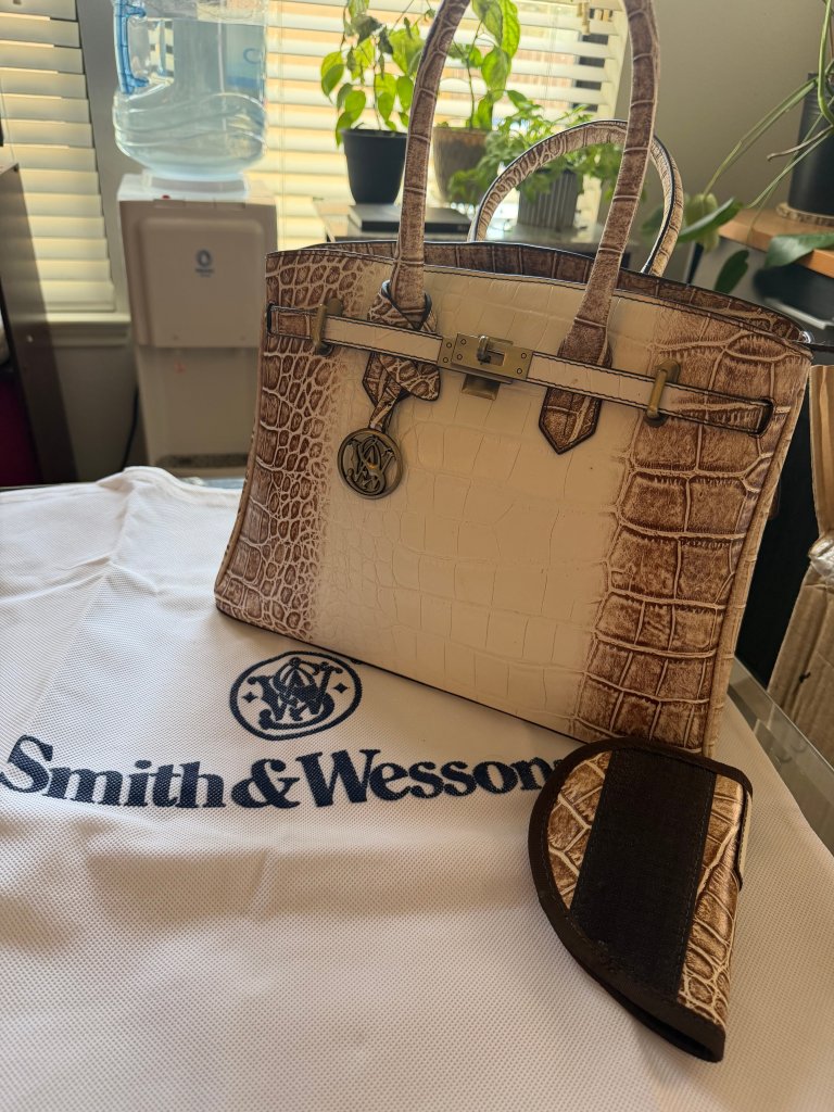 A stylish handbag with a crocodile texture in light brown, featuring a metallic closure and an emblem, placed on a white bag with the 'Smith & Wesson' logo, alongside a matching small pouch.