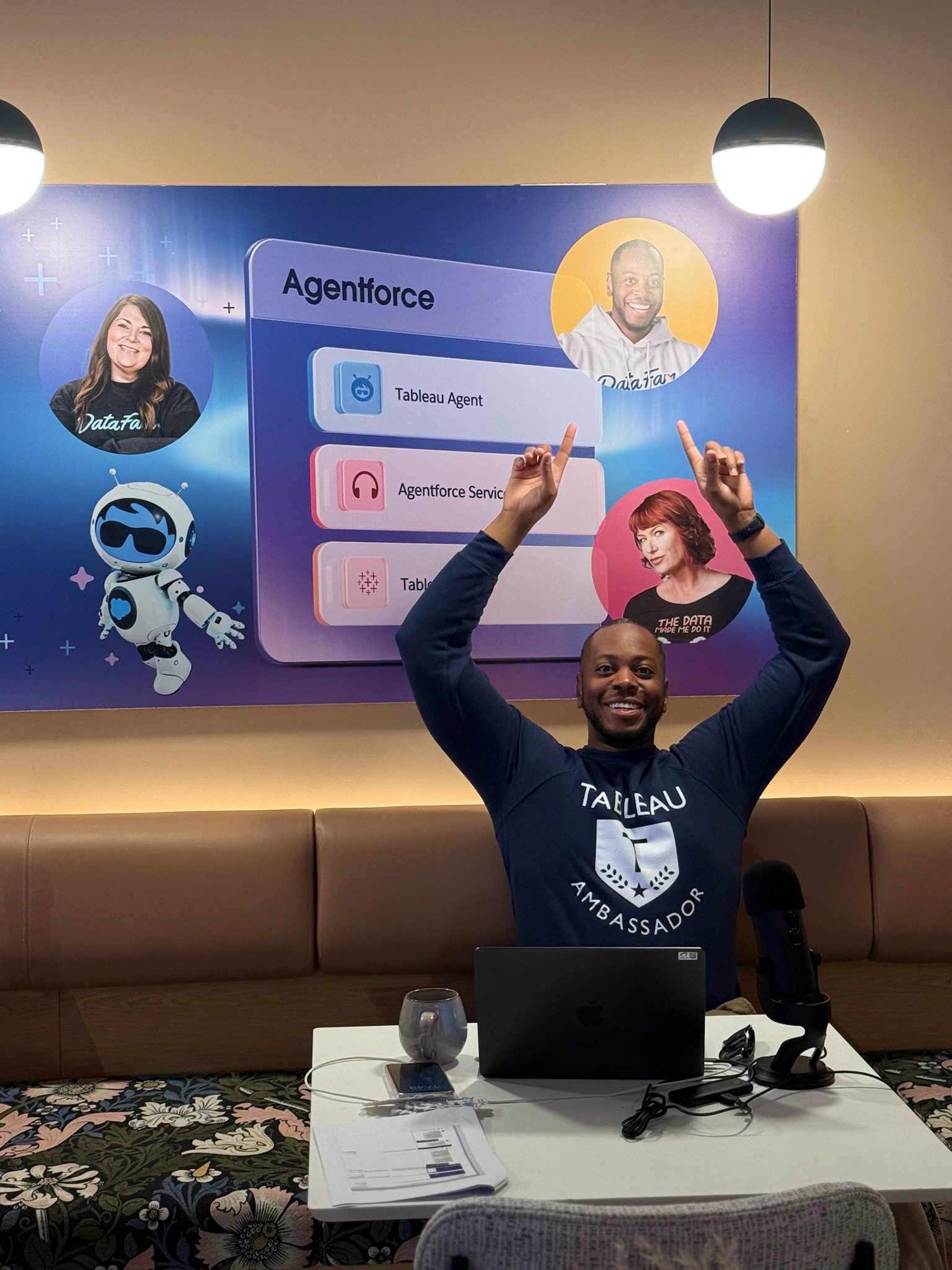 Sekou Tyler with both arms raised behind a laptop, an Agentforce and Tableau Agent slide on the screen behind him, wearing a Tableau Ambassador sweatshirt