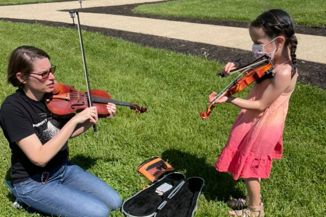 Child with violin teacher taking an outdoor lesson.