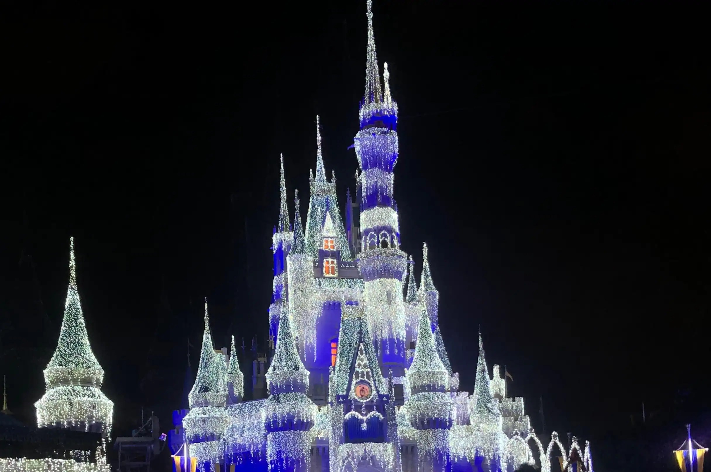 Cinderella Castle glowing with shimmering white and blue Christmas lights during Disney at Christmas at Magic Kingdom.