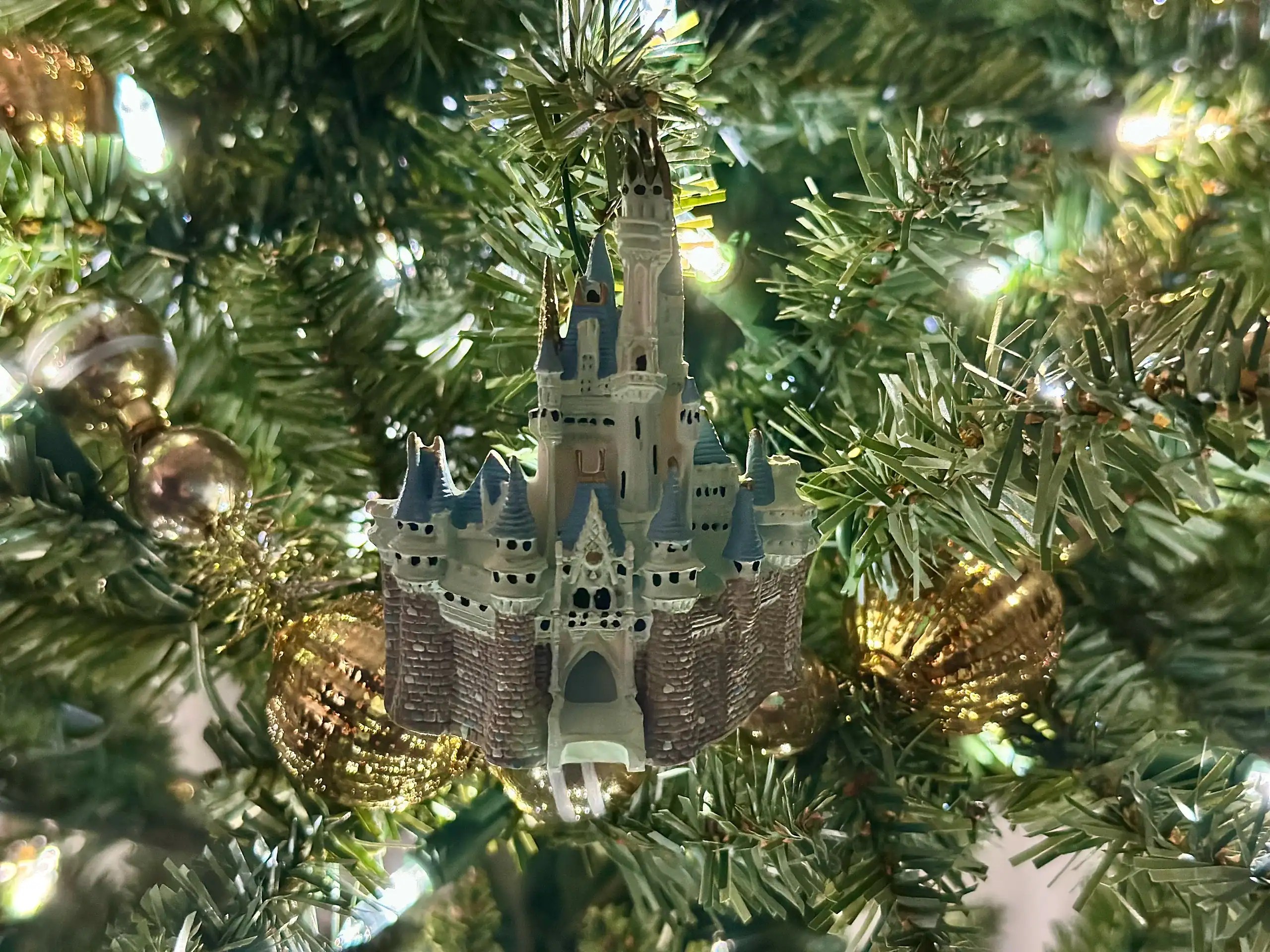 Close-up of a Disney castle Christmas ornament glowing on a lit tree for a Disney holiday gifts for kids guide.