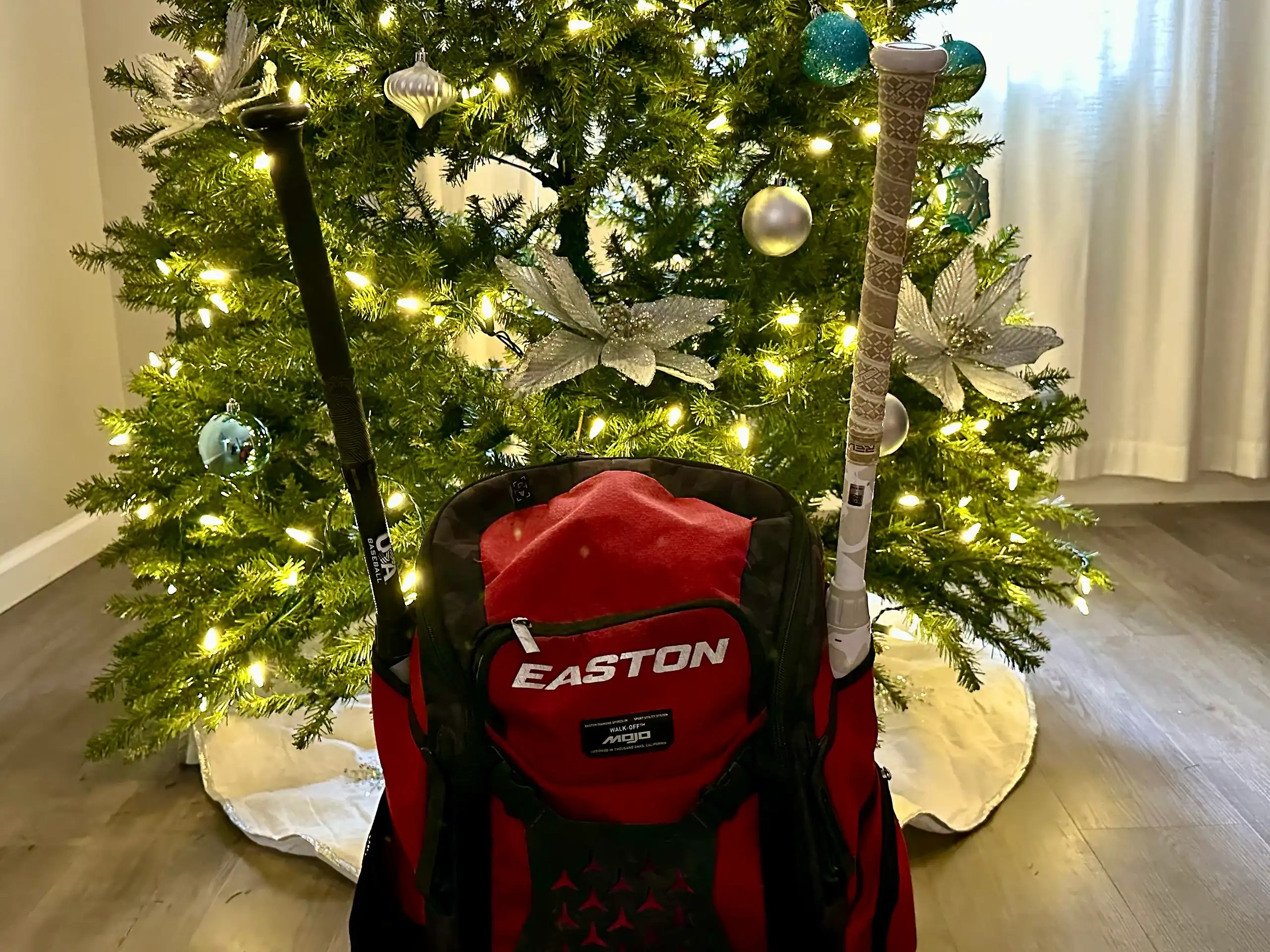 Youth baseball bag with bats in front of a Christmas tree, featuring practical baseball gift ideas for kids and teens