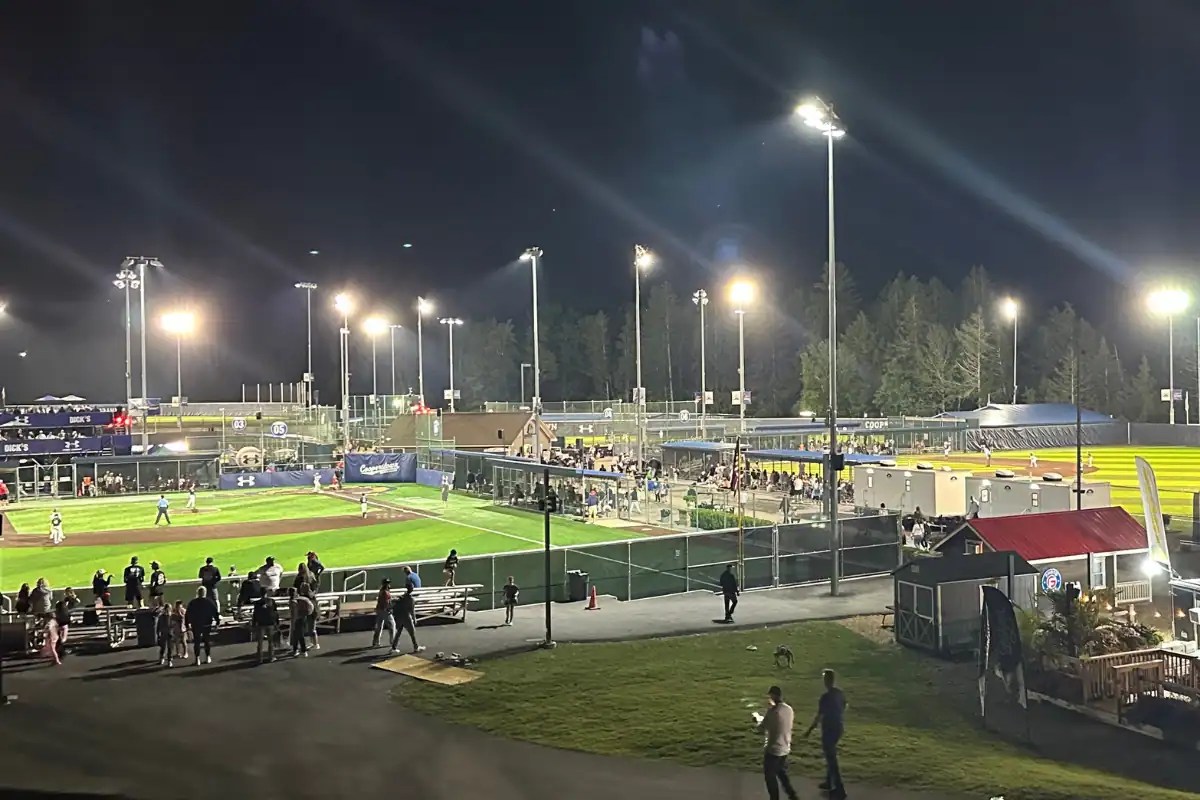 Overview of Cooperstown All Star Village during evening tournament games showing multiple baseball fields and families around the complex