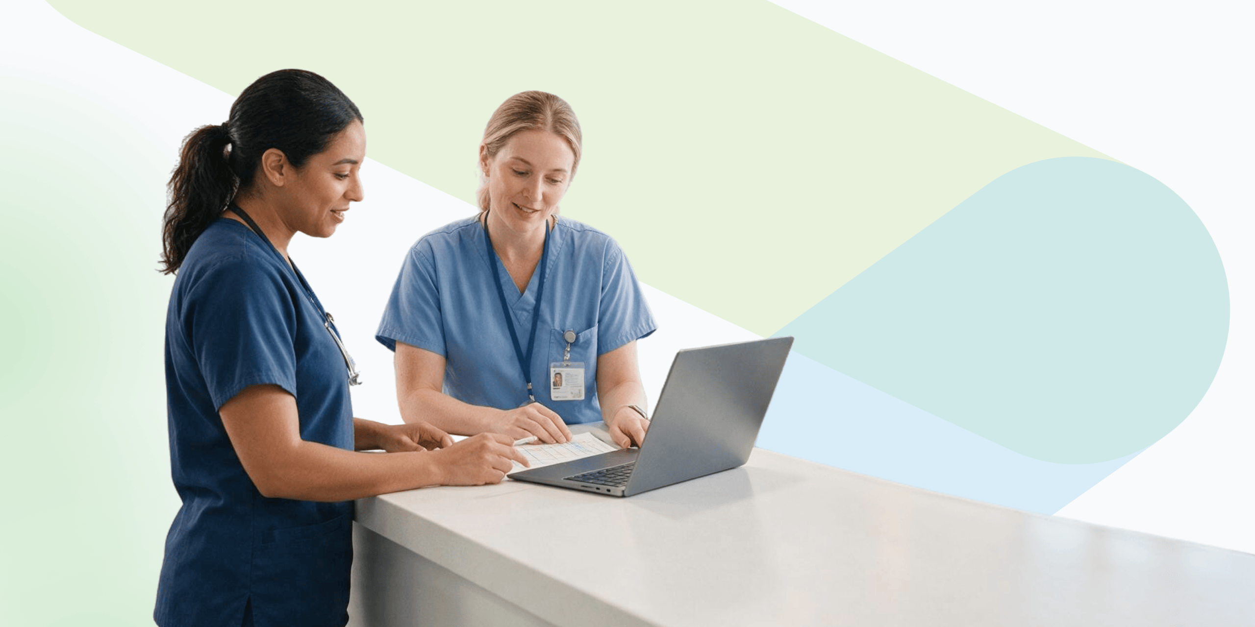 Two nurses reviewing a shift schedule on paper and a laptop at a hospital counter
