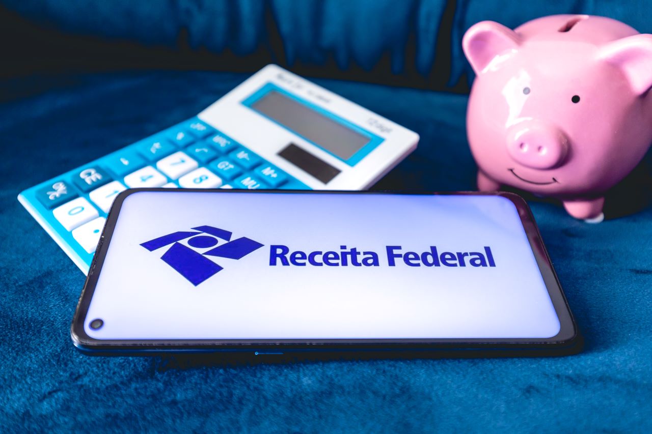 Como doar parte do Imposto de Renda para entidades? | Foto de um celular com o logo do site da Receita Federal, uma calculadora e um cofrinho de porquinho rosa | Certificação Digital | Blog da Certisign