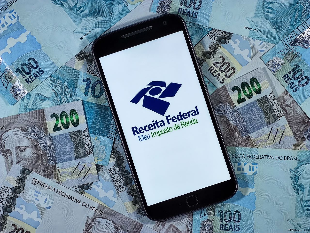O que é malha fina? | Foto de um celular no app da Receita Federal em cima de várias notas de cem e duzentos reais | Certificação Digital | Blog da Certisign