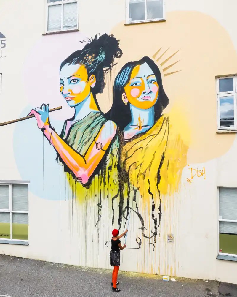Painted wall with two women and the artist painting.
