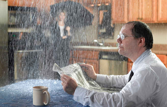 Image of man reading paper with a leaking roof