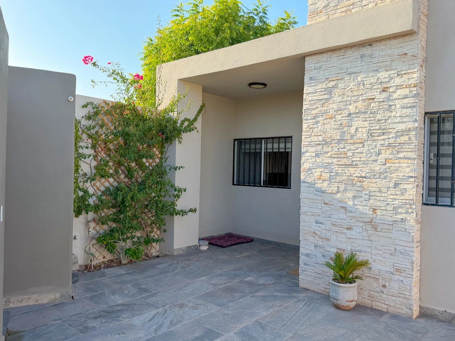 Entrada techada de Casa Xantus con columna de piedra laja y buganvilia