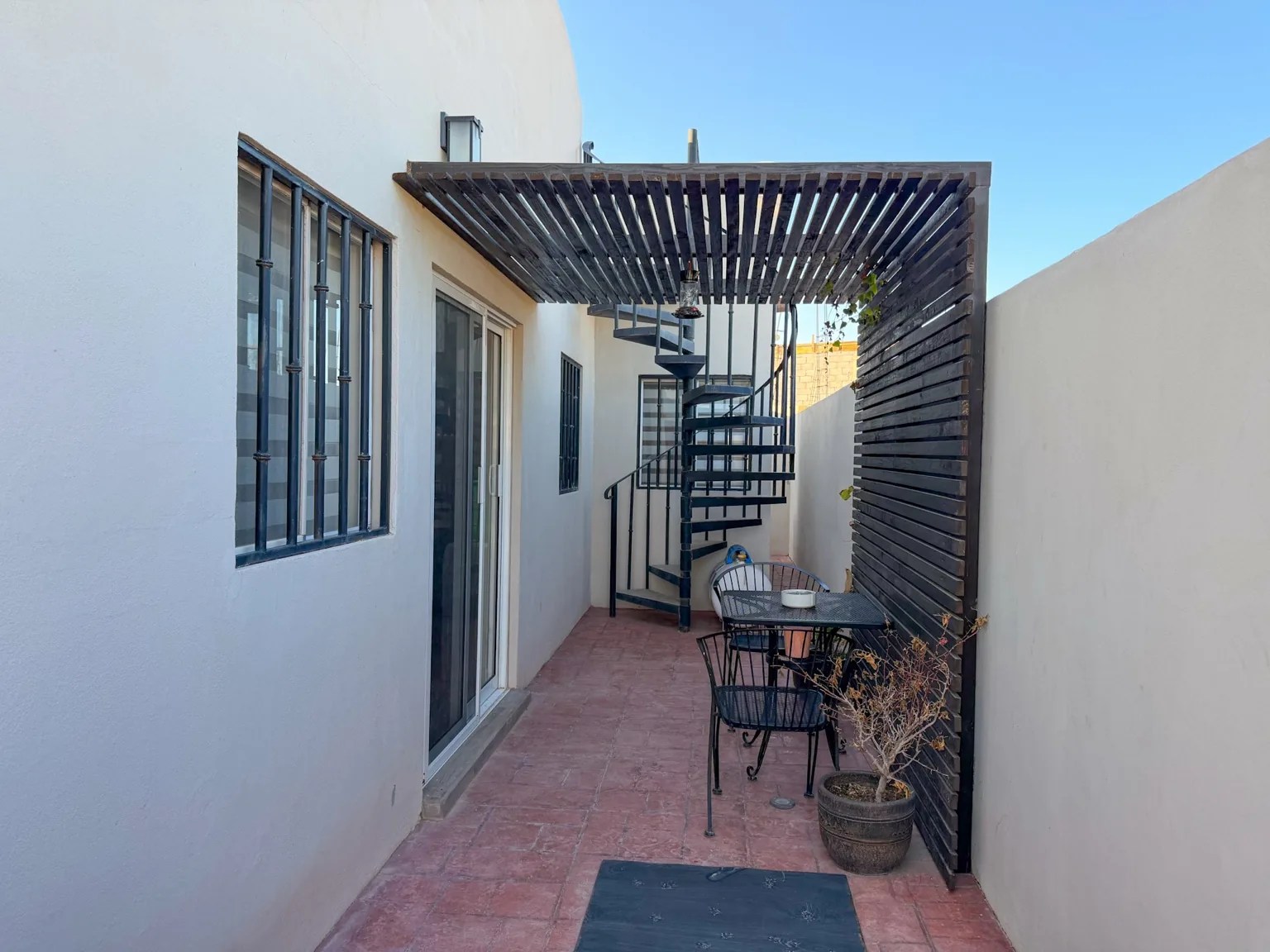 Patio lateral techado de Casa Xantus con pérgola de madera y escalera de caracol hacia la terraza