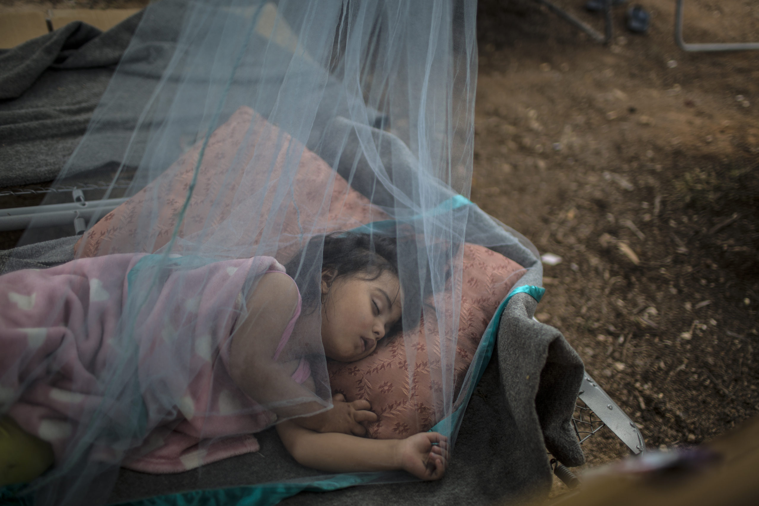Anna Rahmoni, an almost 2-year-old Afghan refugee child sleeps under a mosquito net outside her family's tent to escape the heat trapped inside at Malakasa refugee camp north of Athens, Greece..