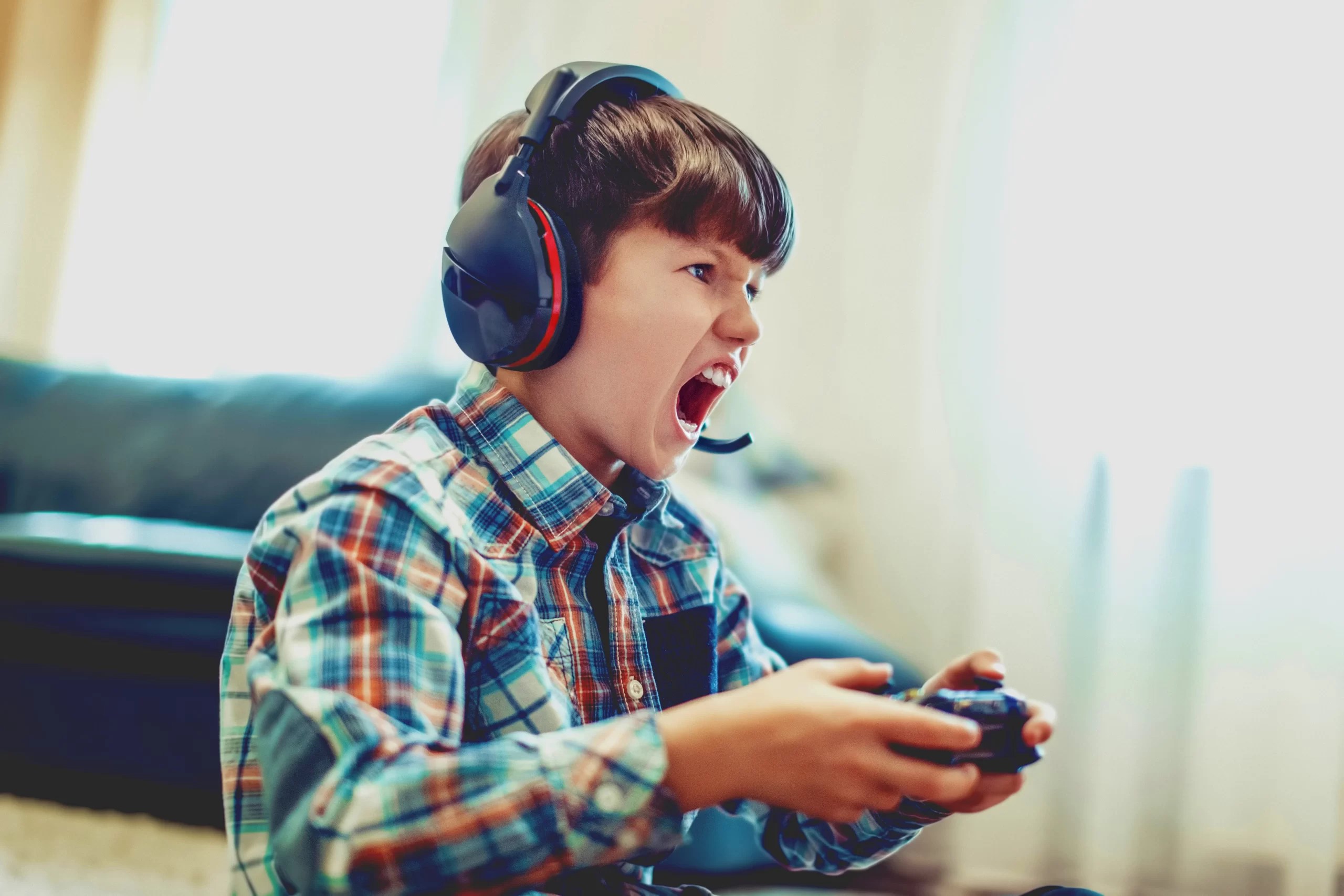 Boy with his headphones on and controller in his hand experiencing behavior change and is screaming at whatever is happening on his screen.