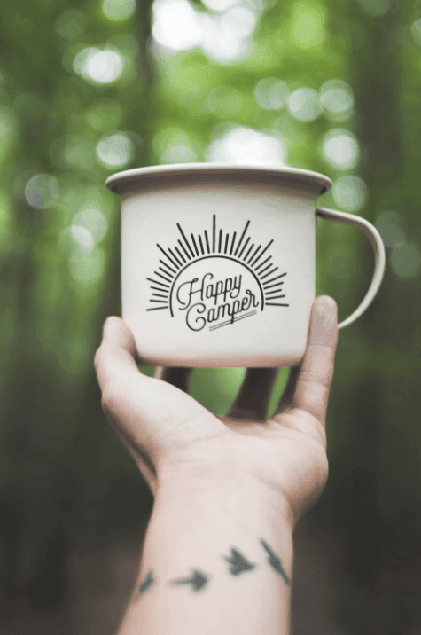Happy cycle camping! A hand holding up a tin mug, with Happy Camper printed on it