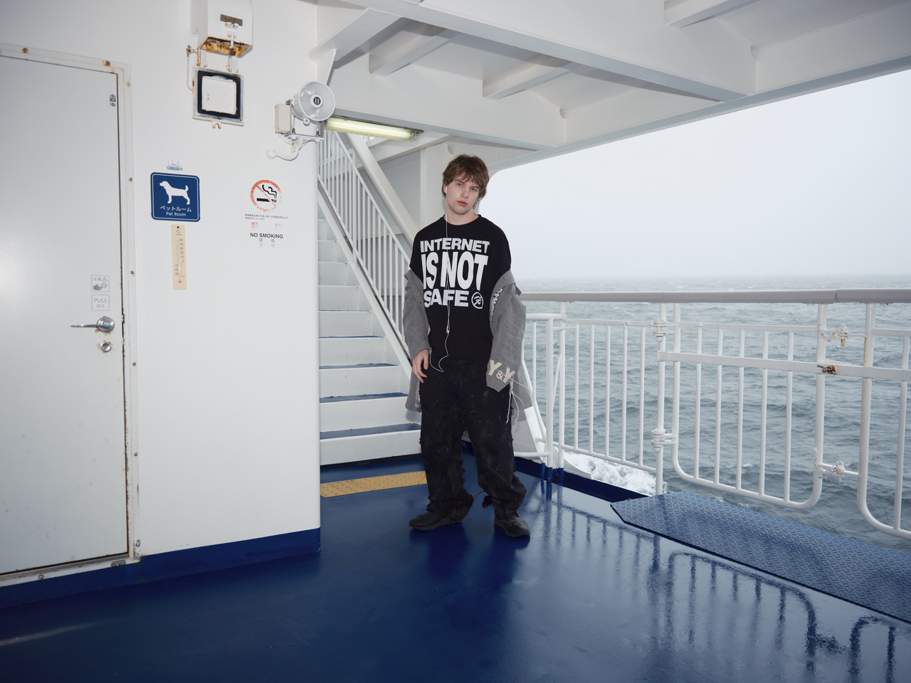 Øneheart pictured on a ferry wearing in-ear headphones and a black T-shirt in a promotional image for his new single, “internetisNOTsafe”.