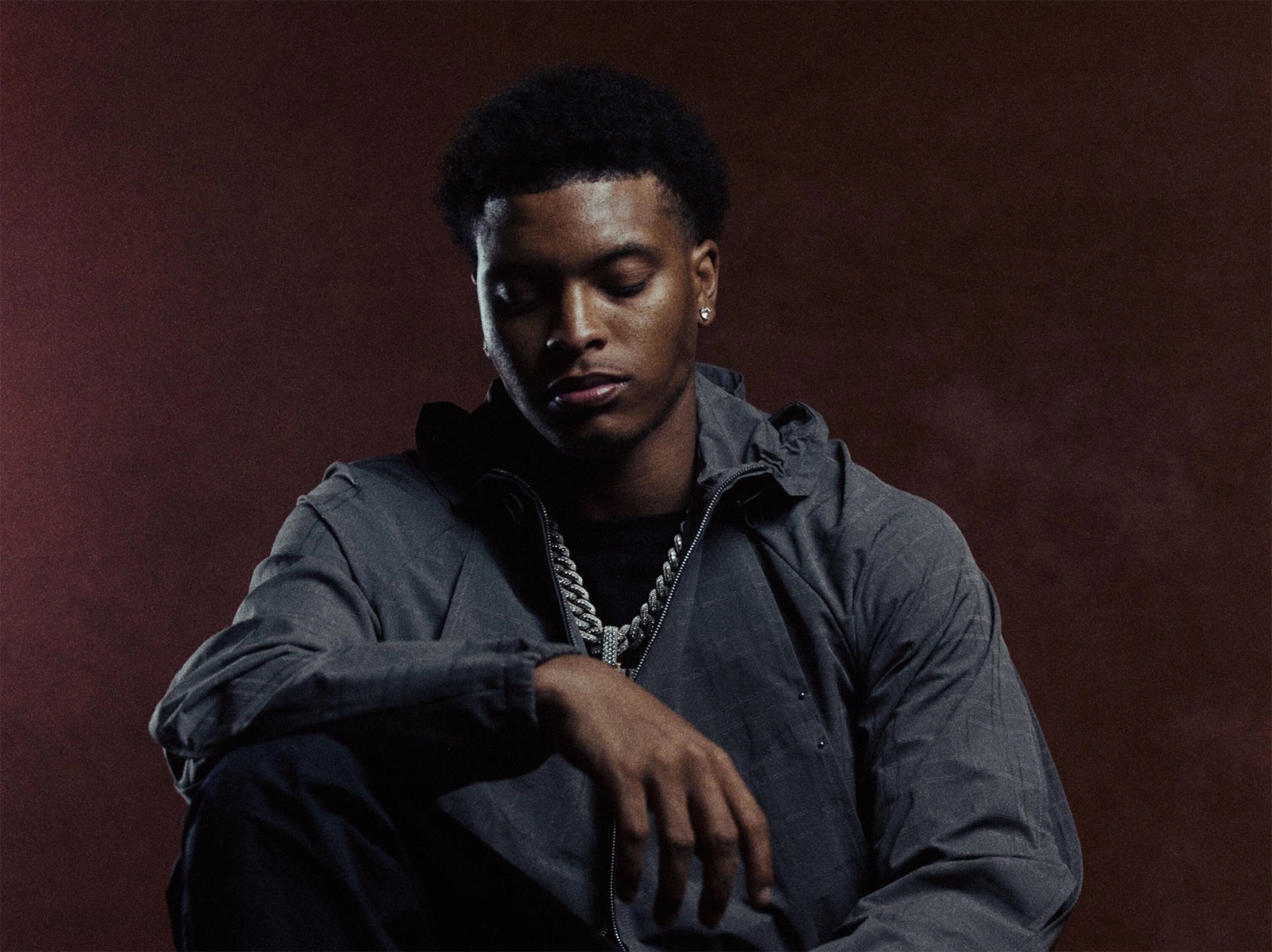 Nemzzz pictured looking down against a maroon backdrop in a promotional photo.