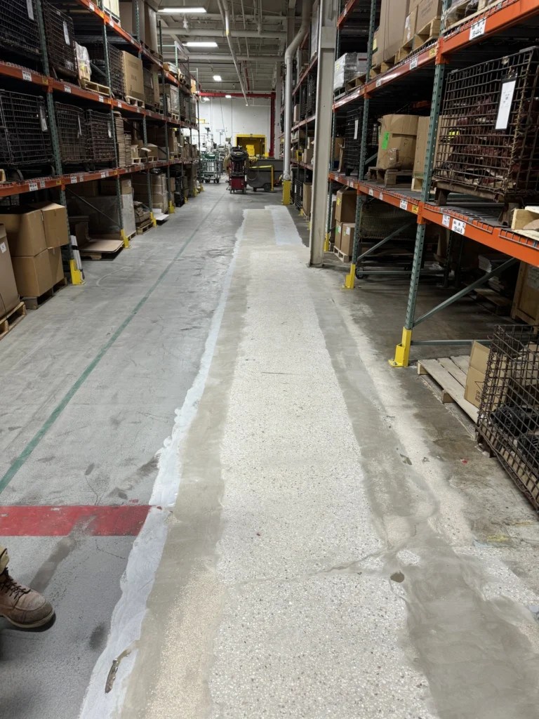 Durable industrial warehouse floor with light gray coating and green safety lines, shelves stocked with boxes