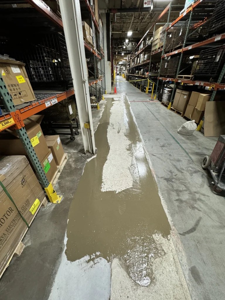 Unfinished concrete floor coating repair project in a warehouse with shelves of products and materials