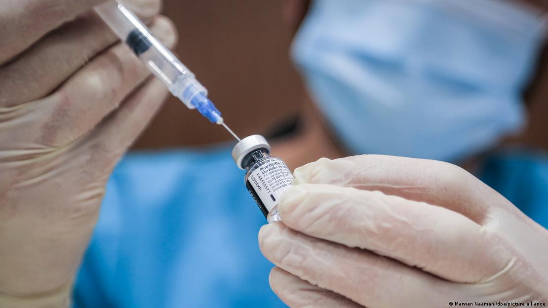 Una persona con guantes médicos intoduce una jeringa en un frasquito.
