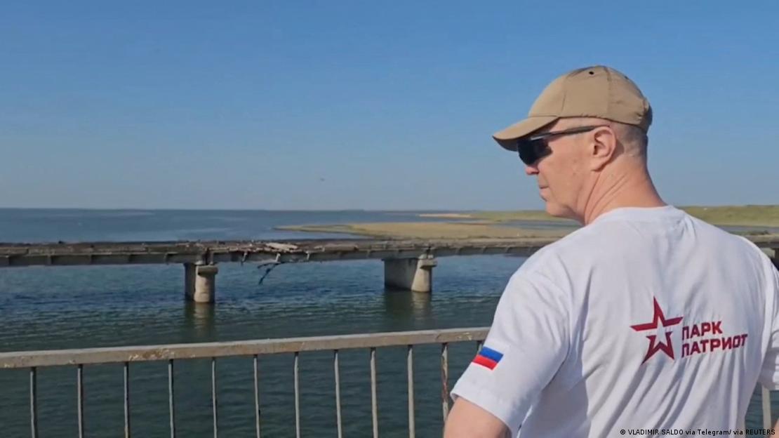 Se ve al gobernador ruso con gorra y gafas de sol de perfil mirando desde una varandilla hacia el puente dañado.