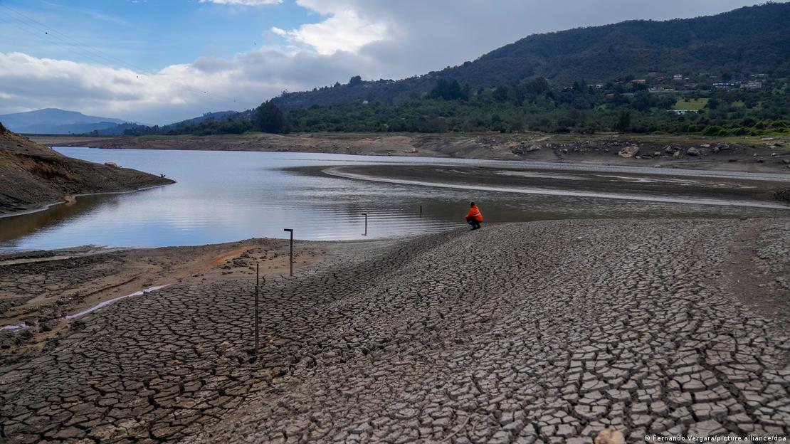 Uh hombre sentado frente a una reserva de agua potable en disminución por la sequía en Colombia.