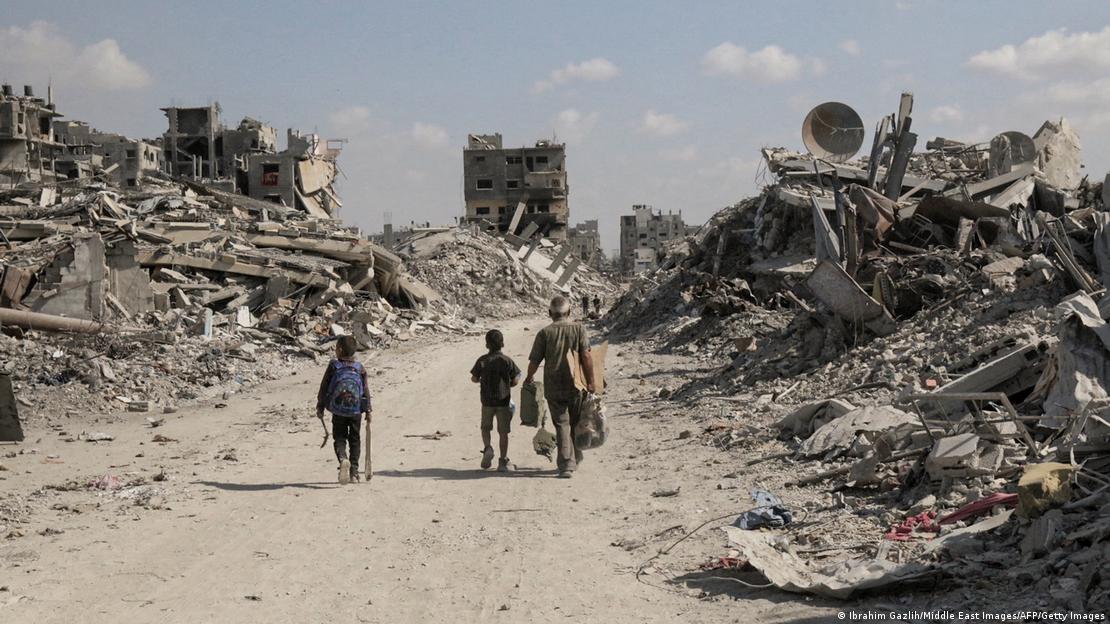 Territorios Palestinos, Jan Yunis, 2025 | Un adulto y dos menores regresan a la ciudad destruida, por un camino, con montañas de escombros a ambos lados.