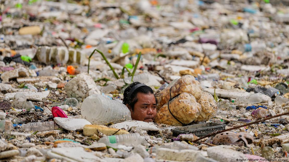 Un trabajador retira basura de un canal de agua, con el agua y basura hasta el cuello, tras las intensas lluvias del monzón en Filipinas.