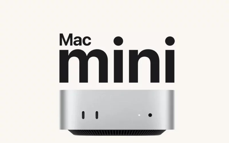 銀色 Mac mini 放置在辦公桌，背景螢幕顯示六月出貨的資訊。