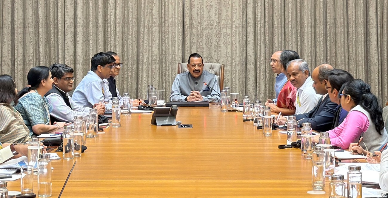 A meeting with multiple participants seated around a large conference table, with a central figure addressing the group.