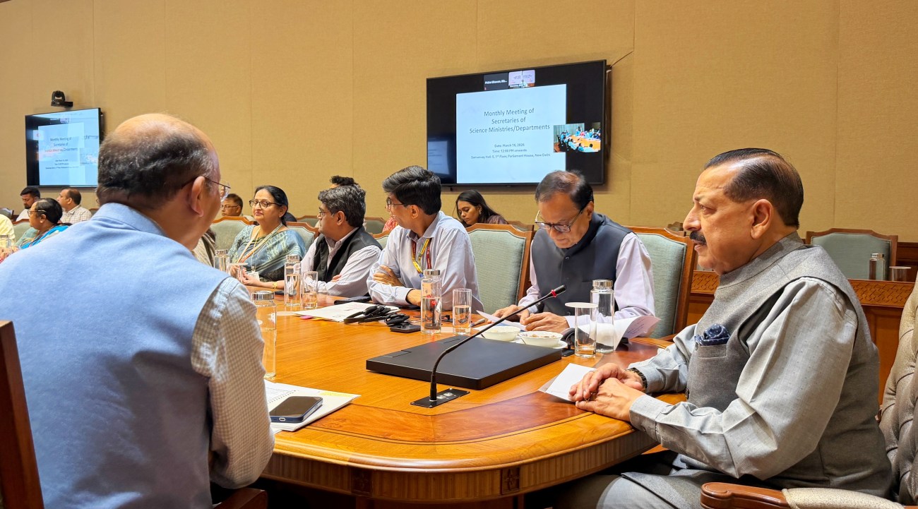A meeting of various officials discussing topics related to science ministries and departments, seated around a large wooden table with water glasses and documents present.