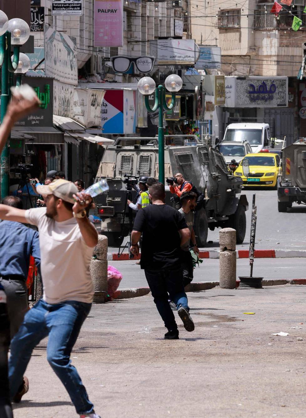 فلسطينيون يرشقون مركبات للجيش الإسرائيلي في أثناء مداهمة في نابلس بالضفة الغربية أمس (أ.ف.ب)