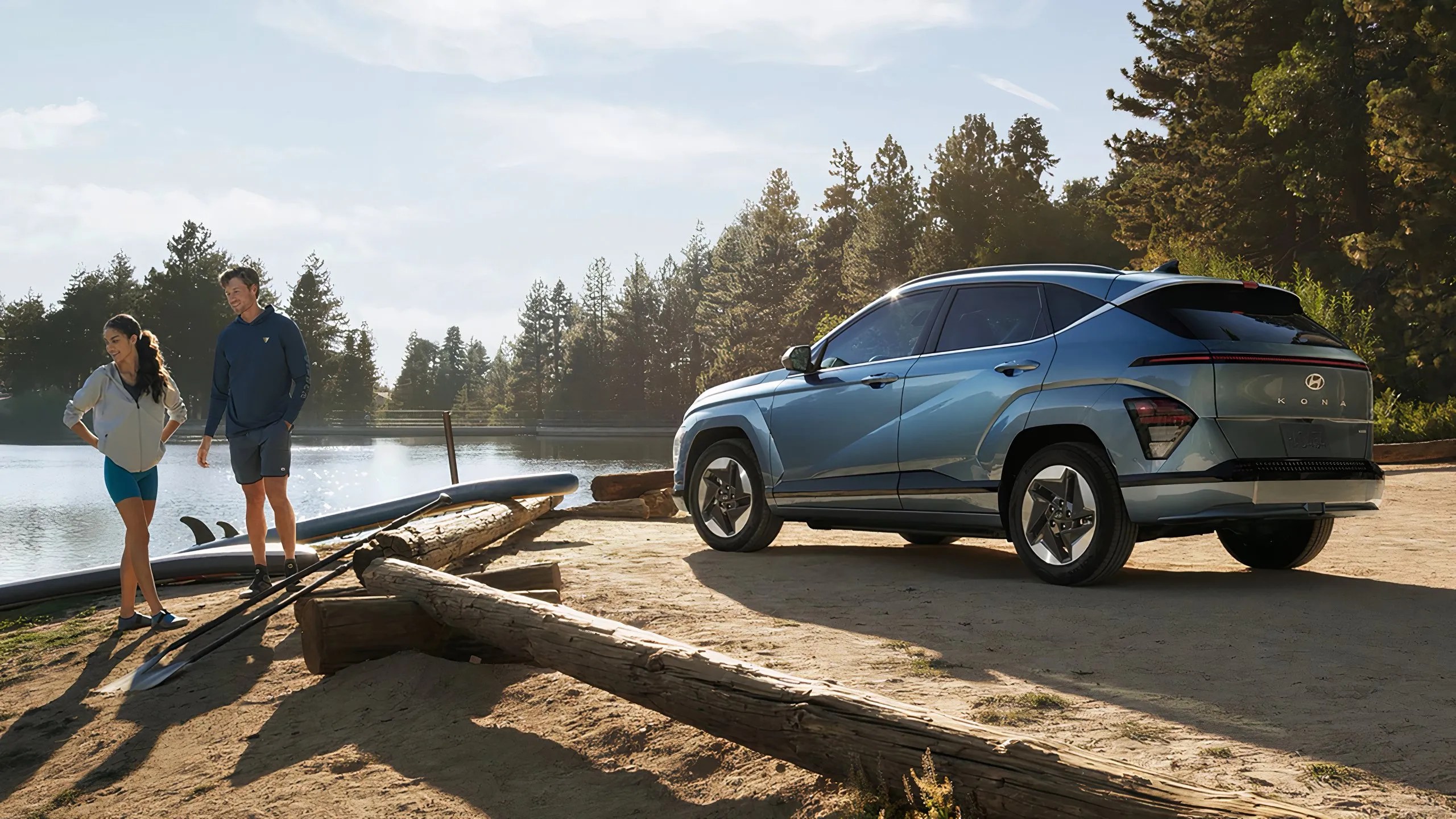 Une photo immobile d'une électrique Hyundai Kona garée à côté d'un lac et de deux personnes. 