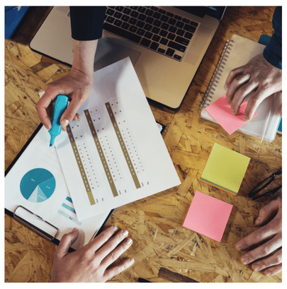Image of people hands on a table with analytical graphs, sticky notes, and a laptop. The image is over the free resource library which contains data analysis, statistical analysis, and business insight resources for visitors to our site.
