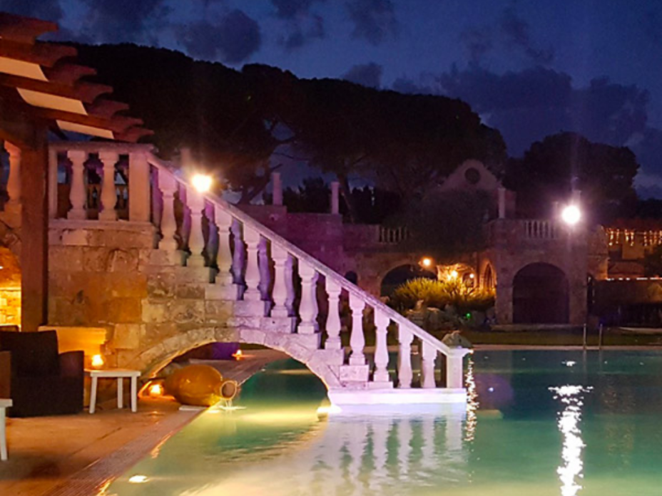 Beleuchteter Pool mit Steinbrücke im Tenute Al Bano Carrisi bei Nacht.