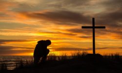 Beautiful sunset as man bows down to pray God before a cross.