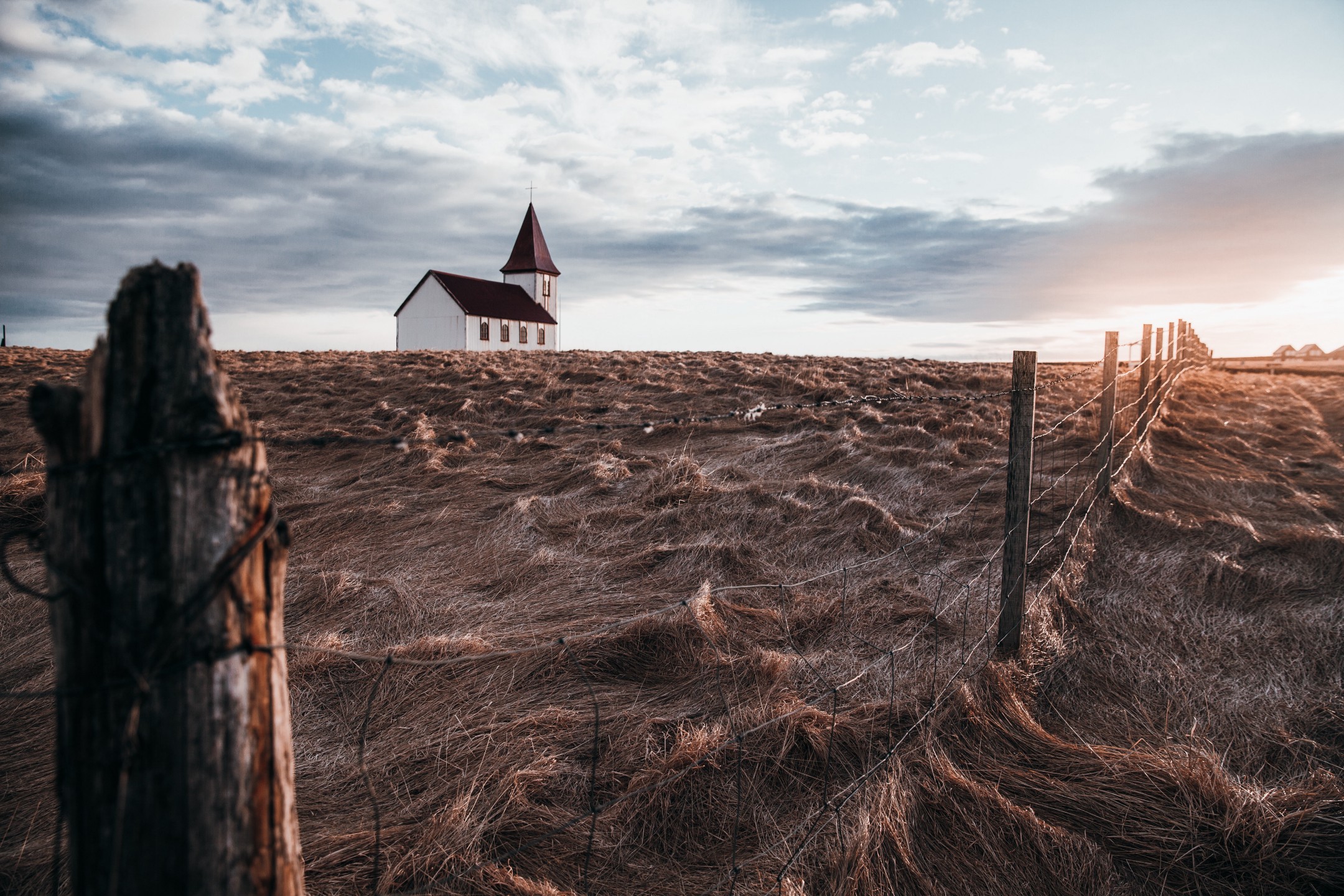 church building in an empty field. The sky is gloomy. A fence runs down the right side of the picture.