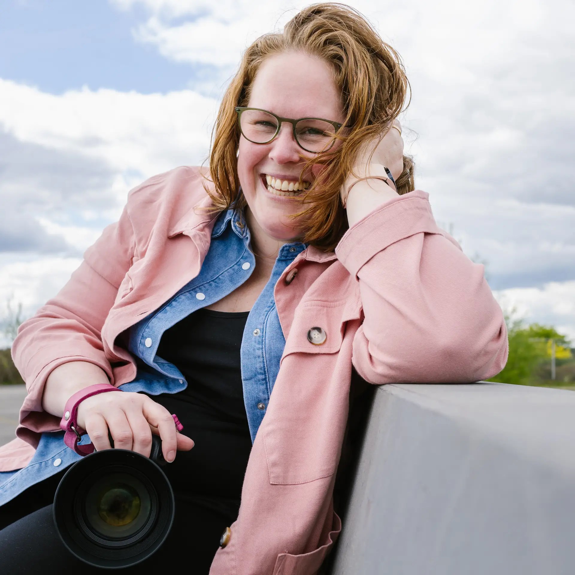 Stephanie, fotograaf in Hilversum, draagt een roze blouse en houdt haar camera vast tijdens een portretfoto.